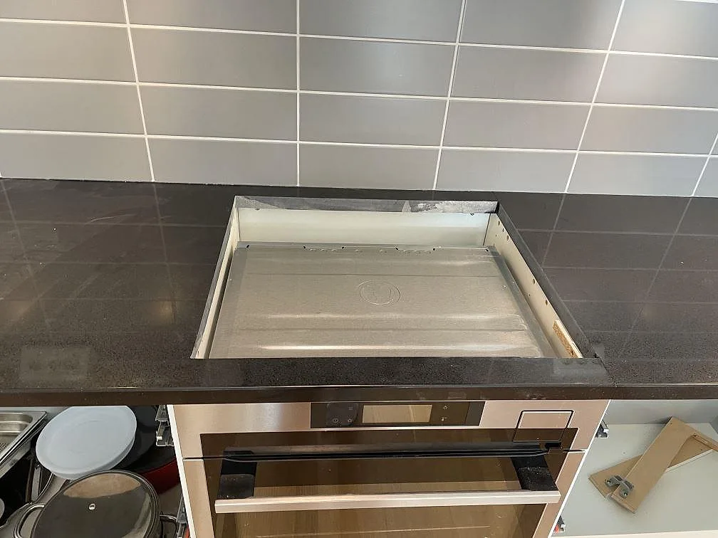 Hälluttag i köksbänkskiva av polerad Technistone Gobi Black komposit ovanför ugn och grått kakel i Dalby.