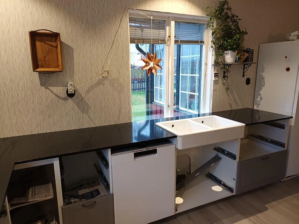 Närbild av svart polerad Technistone Gobi Black bänkskiva vid vit dubbelho och fönster i kök i Eskilstuna.