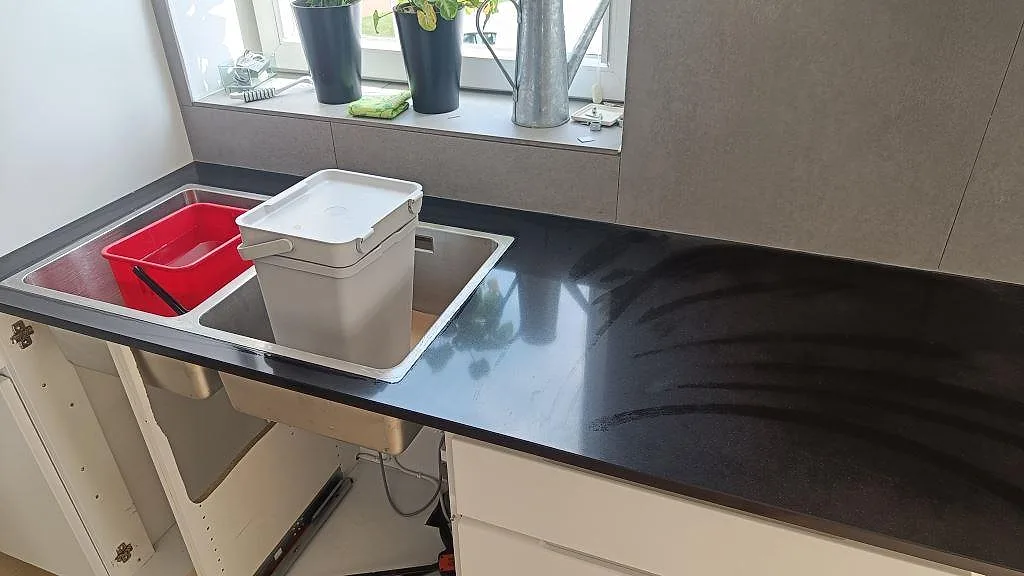 Köksbänkskiva i svart Technistone Gobi Black, polerad, med rostfri dubbelho vid fönster i ett kök i Göteborg.