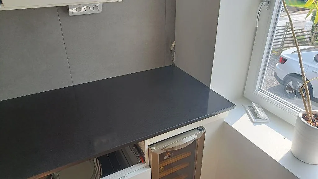 Sidobänk i svart polerad Technistone Gobi Black vid fönster och väggbeklädnad i ett kök i Göteborg.