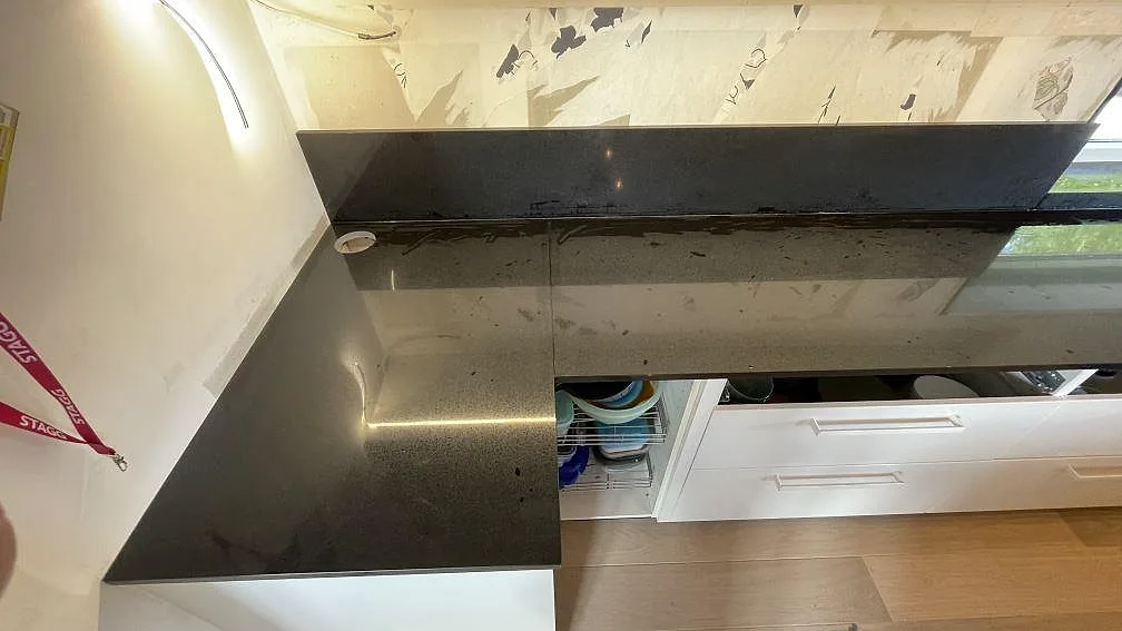 Svart polerad väggbänk i Technistone Gobi Black med stänkkant och finkornig komposityta under montering i Kalmar.
