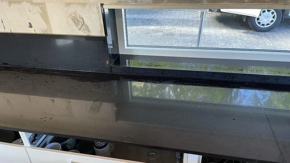 Polerad svart köksbänkskiva i Technistone Gobi Black under fönster, med låg stänkkant och tydliga reflektioner i Kalmar.