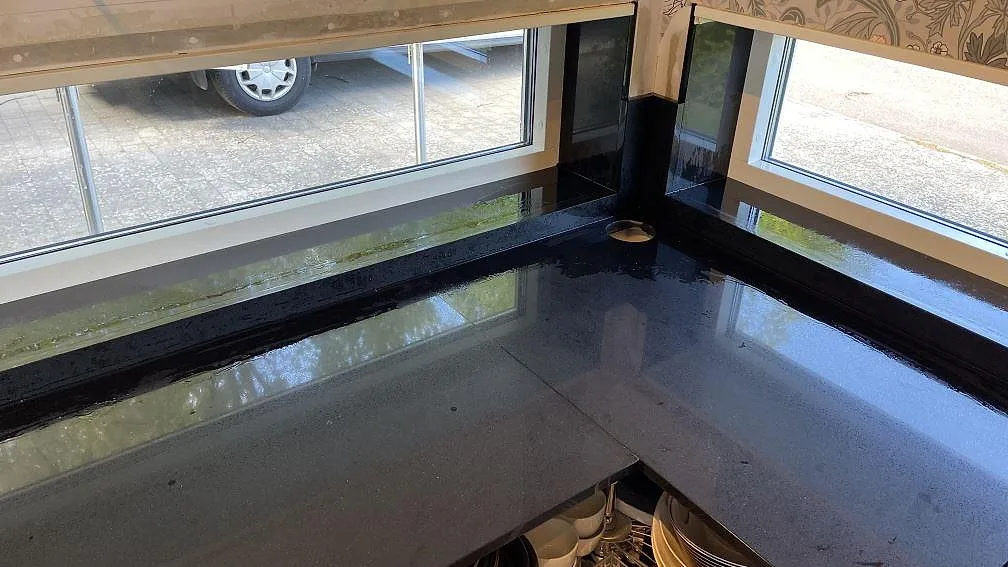 L-formad väggbänk i Technistone Gobi Black, polerad svart kvartskomposit, med uppvikt stänkkant vid hörnfönster i Kalmar.