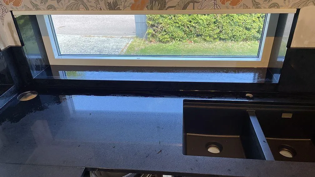 Svart polerad Technistone Gobi Black bänkskiva med dubbelho och låg stänkkant vid fönster i ett kök i Kalmar.
