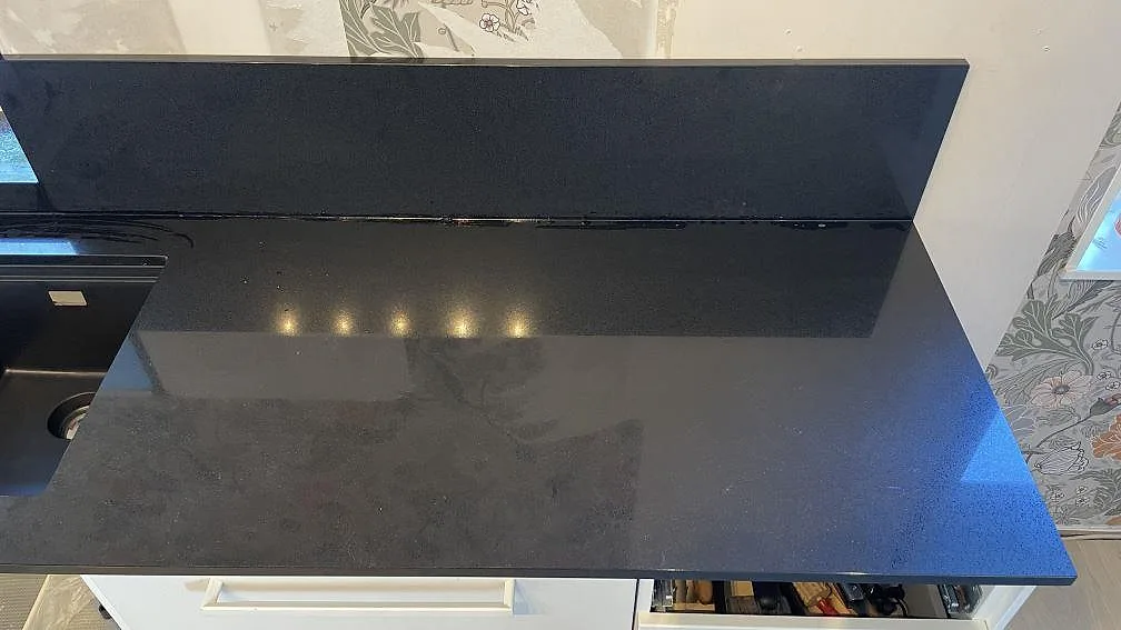 Detalj av Technistone Gobi Black bänkskiva med låg stänkkant och blank polerad yta bredvid diskhon i Kalmar.