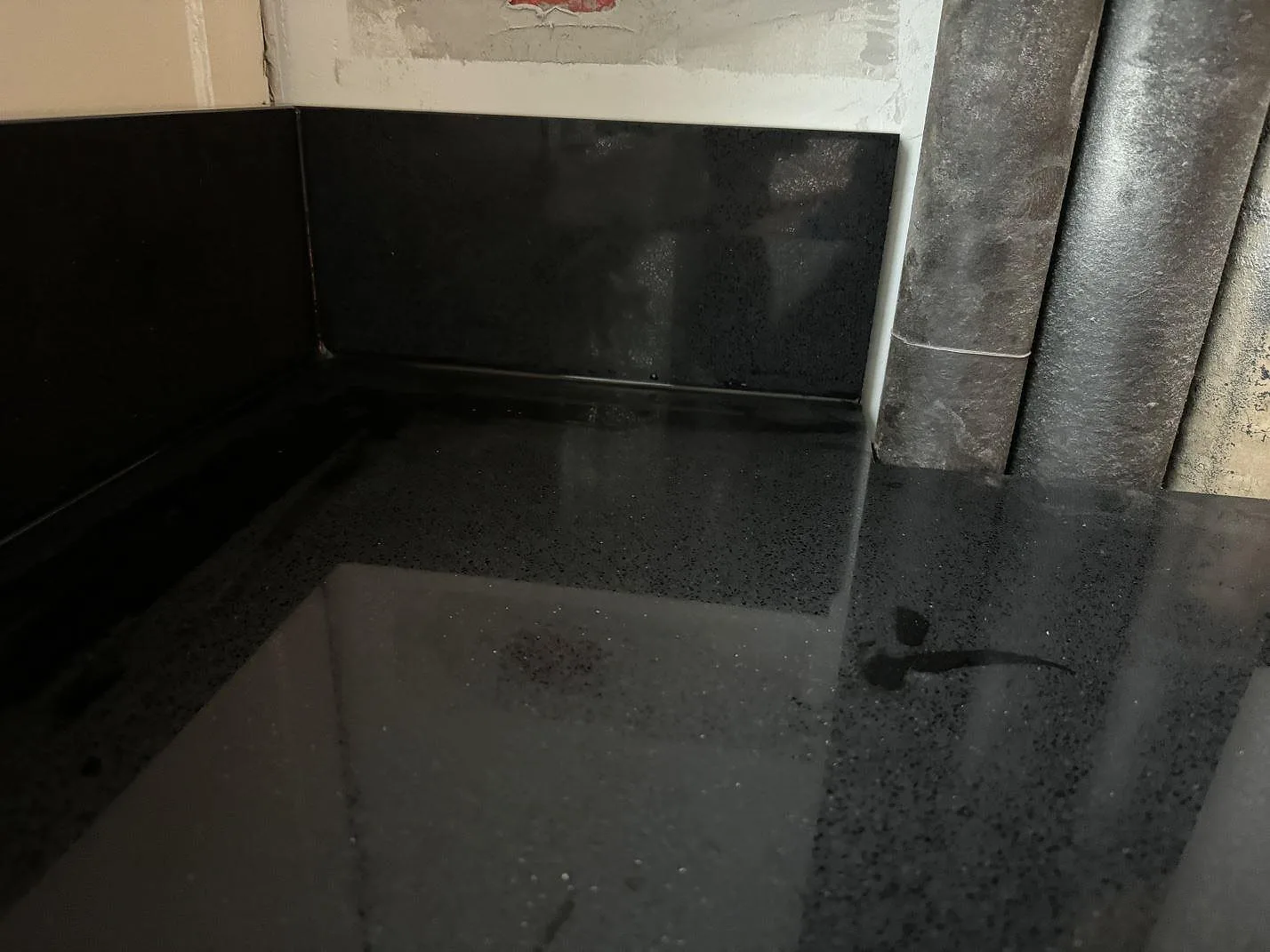 Närbild på blank svart Technistone Gobi Black komposit med uppvikt stänkkant under köksmontering i Kastrup.