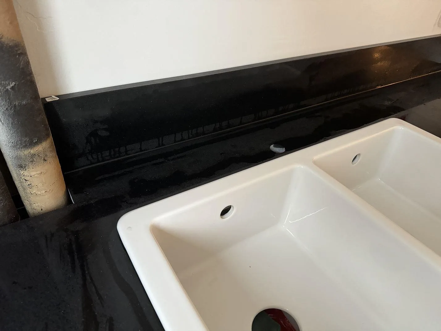 Närbild på vit dubbelho och svart polerad Technistone Gobi Black bänkskiva med stänkkant i Kastrup.