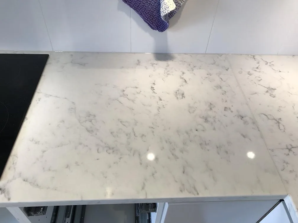 Köksbänkskiva i Technistone Mystery White i Åhus, polerad yta med mjuk grå ådring och infälld induktionshäll i kanten.