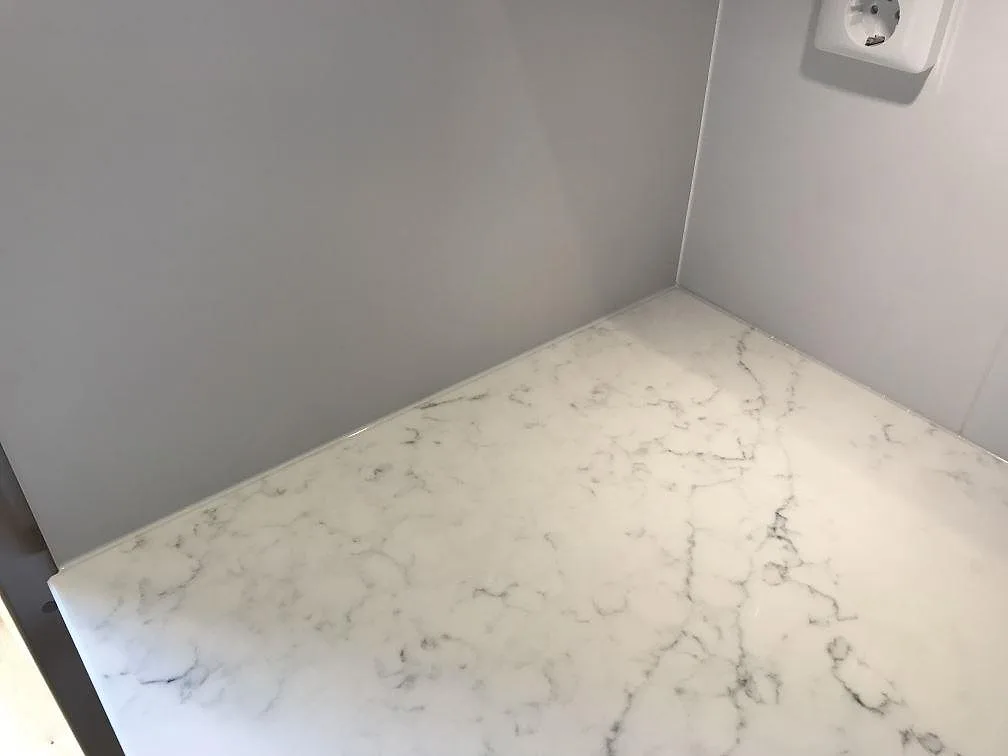 Närbild på den polerade köksbänkskivan i Technistone Mystery White i Åhus, med varmvit botten och fin grå marmorlik ådring.