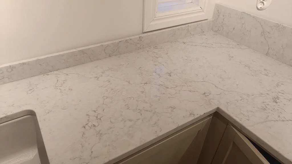 Hörnsektion i polerad Technistone Mystery White med ljus grå ådring och låg stänkkant vid fönstret i Åhus.
