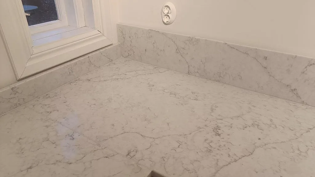 Detalj av polerad Technistone Mystery White på arbetsytan vid fönster och vägguttag, med matchande låg stänkkant i Åhus.