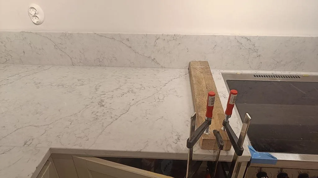 Monteringsbild av spissidan med polerad Technistone Mystery White, induktionshäll, tvingar och låg stänkkant i köket i Åhus.