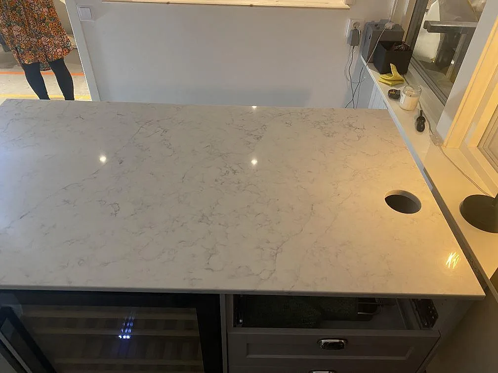 Polerad köksö i Technistone Mystery White med urtag för blandare och rostfri diskho samt vinkyl under i ett kök i Alingsås.