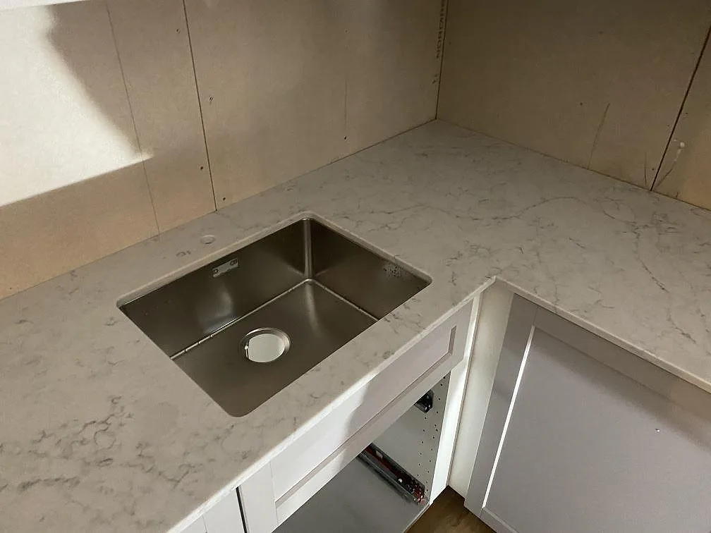 Underlimmad rostfri diskho i en L formad bänkskiva av Technistone Mystery White komposit i ett kök i Alingsås.