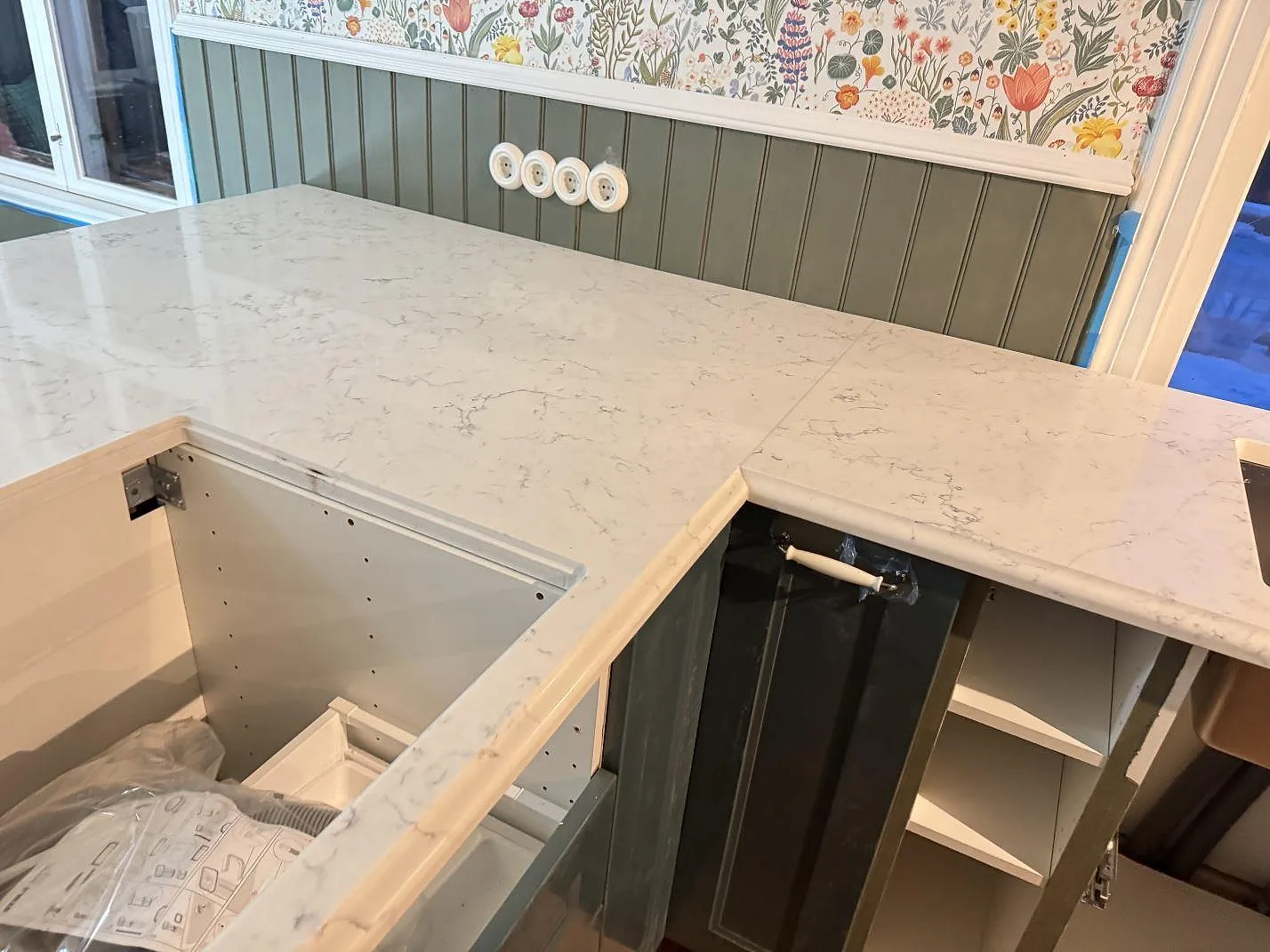 Köksbänkskiva i vit Technistone Mystery White med öppet urtag för diskho och häll under montering i ett kök i Båstad.