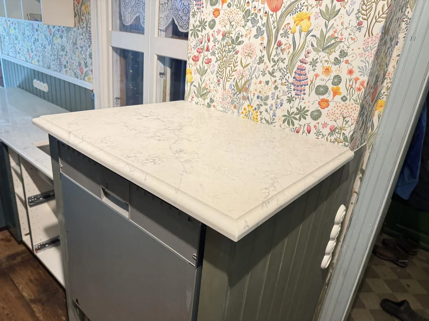 Bänkskiva i Technistone Mystery White med grå ådring på en köksö i salviagrönt i ett kök i Båstad.