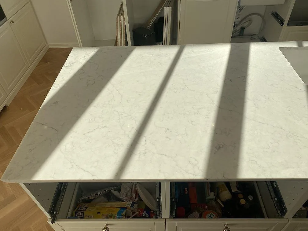 Stänkkant och köksbänkskiva i vit Technistone Mystery White komposit längs fönstervägg i ett kök i Bjärred.