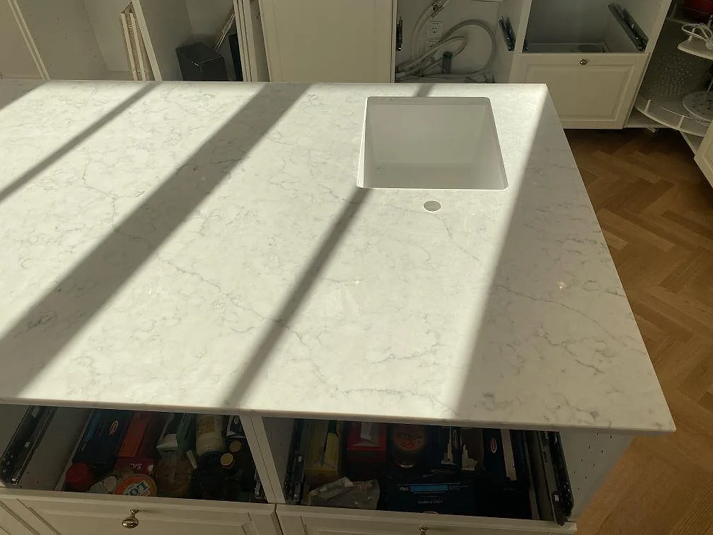 Underlimmad vit diskho i en köksbänkskiva av polerad Technistone Mystery White komposit med grå ådring i ett kök i Bjärred.