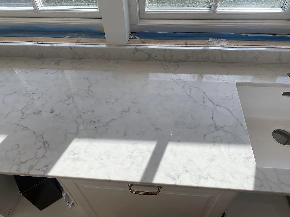 Polerad köksbänkskiva i Technistone Mystery White med matchande fönsterbänk och ådring i dagsljus i ett kök i Bjärred.