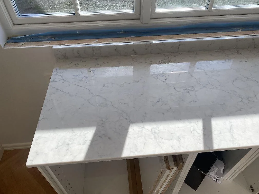Köksbänkskiva i polerad Technistone Mystery White komposit vid fönsterbänk med tydlig grå ådring i ett kök i Bjärred.