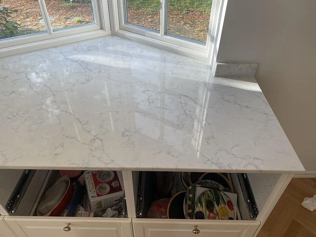 Köksbänkskiva i vit Technistone Mystery White komposit, polerad med grå ådring, monterad i burspråk mot trädgårdsfönster i ett kök i Bjärred.