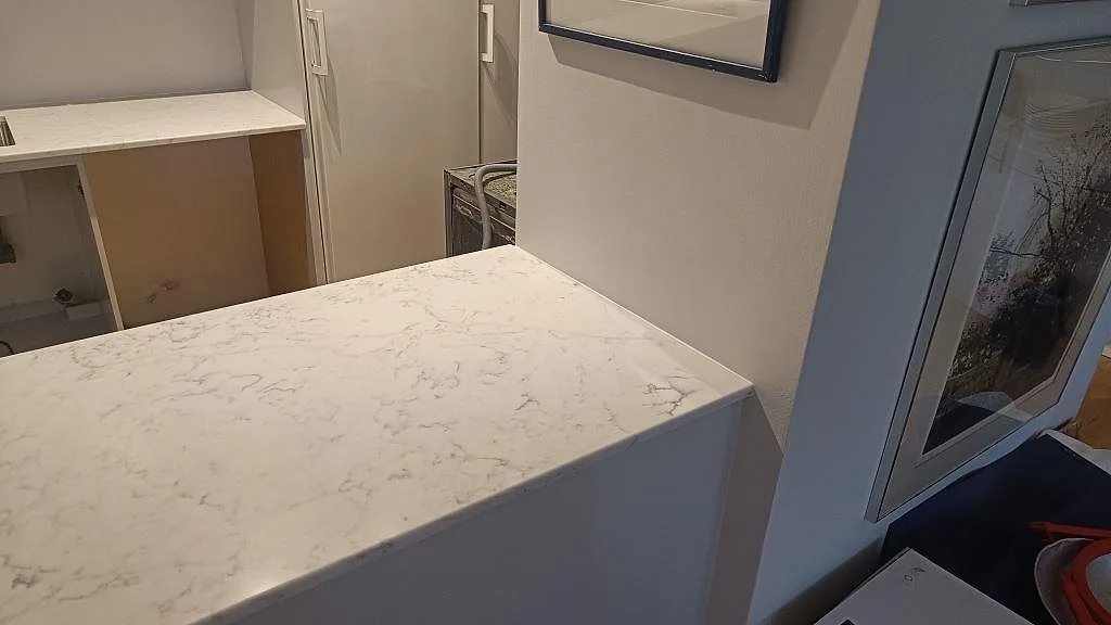 Närbild på köksö i vit Technistone Mystery White, polerad kvartskomposit med grå ådring, i ett kök under montering i Bjärred.