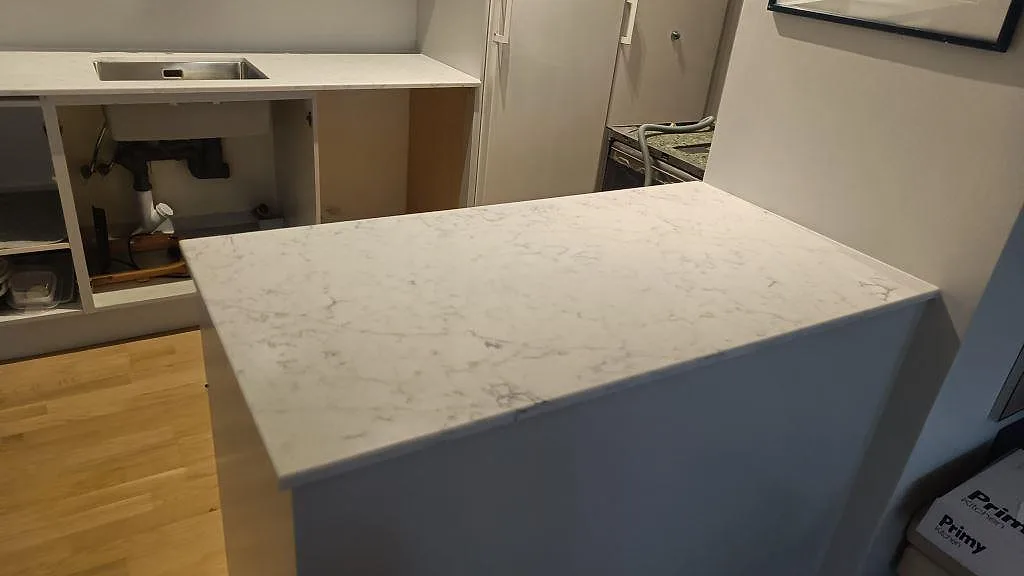 Köksö i Technistone Mystery White med polerad vit komposityta framför bänkrad och rostfri diskho i Bjärred.