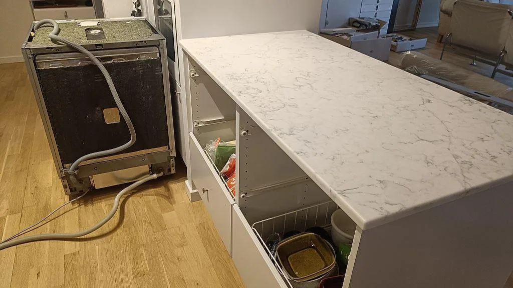 Köksö i polerad Technistone Mystery White med ljus grå ådring och öppna köksstommar under montering i Bjärred.