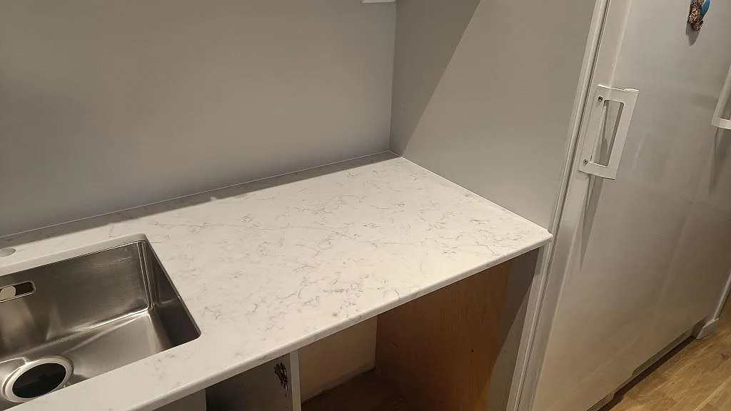 Rak bänkskiva i vit Technistone Mystery White, polerad, vid rostfri diskho och kylskåp i ett kök i Bjärred.