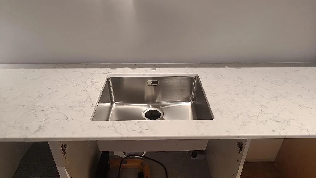 Närbild på polerad Technistone Mystery White-bänkskiva med rostfri diskho, blandarhål och vägganslutning i Bjärred.