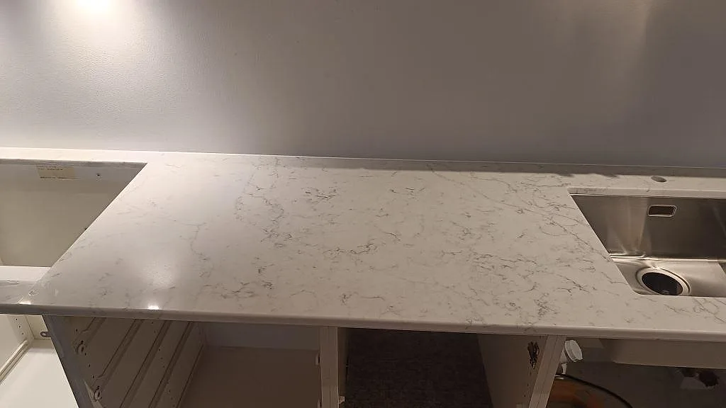 Polerad Technistone Mystery White-bänkskiva mellan rostfri diskho och hällurtag med öppen köksstomme i Bjärred.