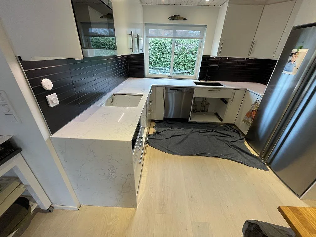 Köksbänkskiva i vit Technistone Mystery White, polerad, i ett U-format kök i Bjärred med mörk kakelfront och underlimmad diskho, fotat under montering.