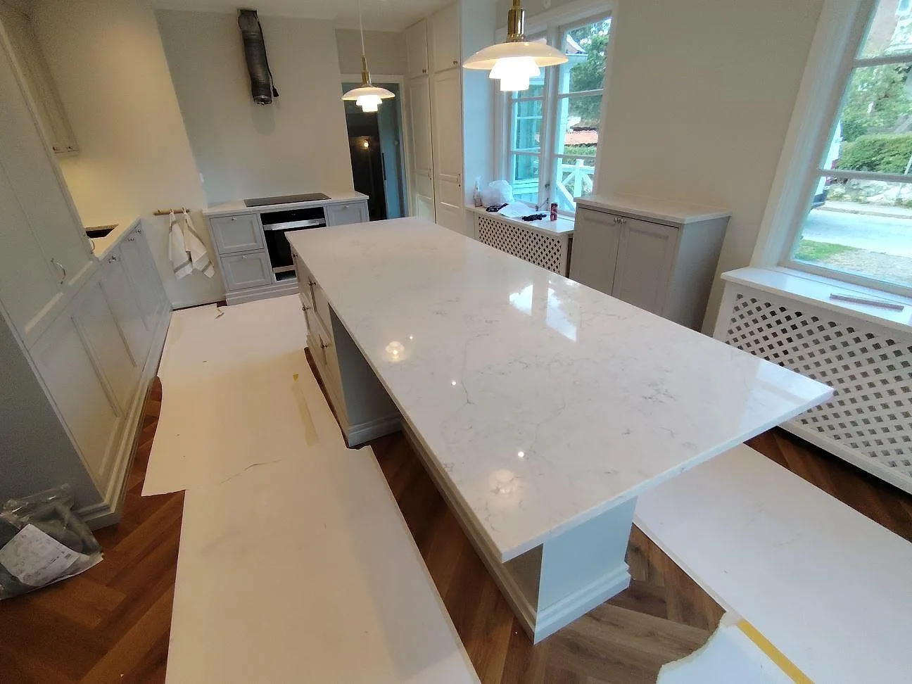 Stor köksö i polerad Technistone Mystery White med ljus ådring, omgiven av grå köksskåp i Bromma.
