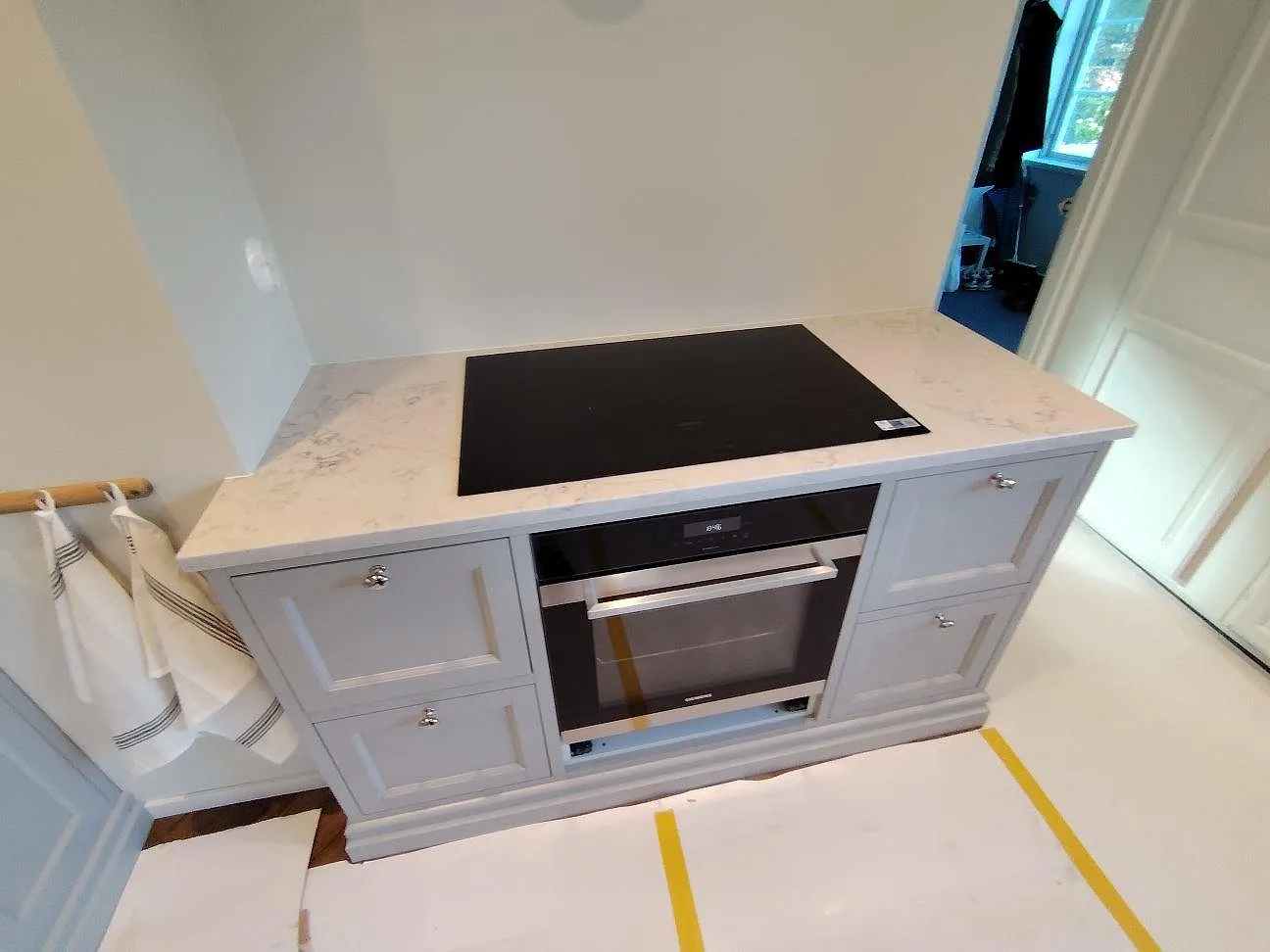 Detalj av köksbänkskiva i polerad Technistone Mystery White med svart häll och inbyggd ugn i Bromma.