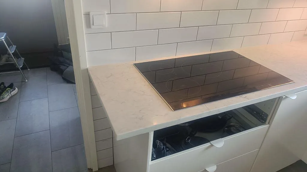 Svart häll monterad i 30 mm polerad Technistone Mystery White ovanför vita kökslådor i Bunkeflostrand.