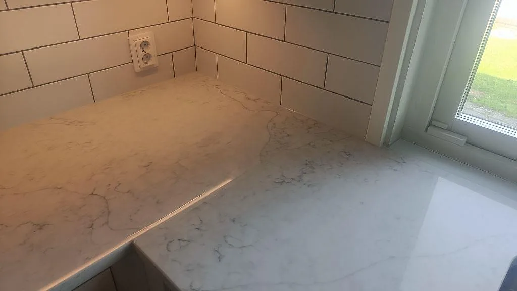 Hörndel av köksbänkskiva i polerad Technistone Mystery White vid fönster och vitt kakel i Bunkeflostrand.