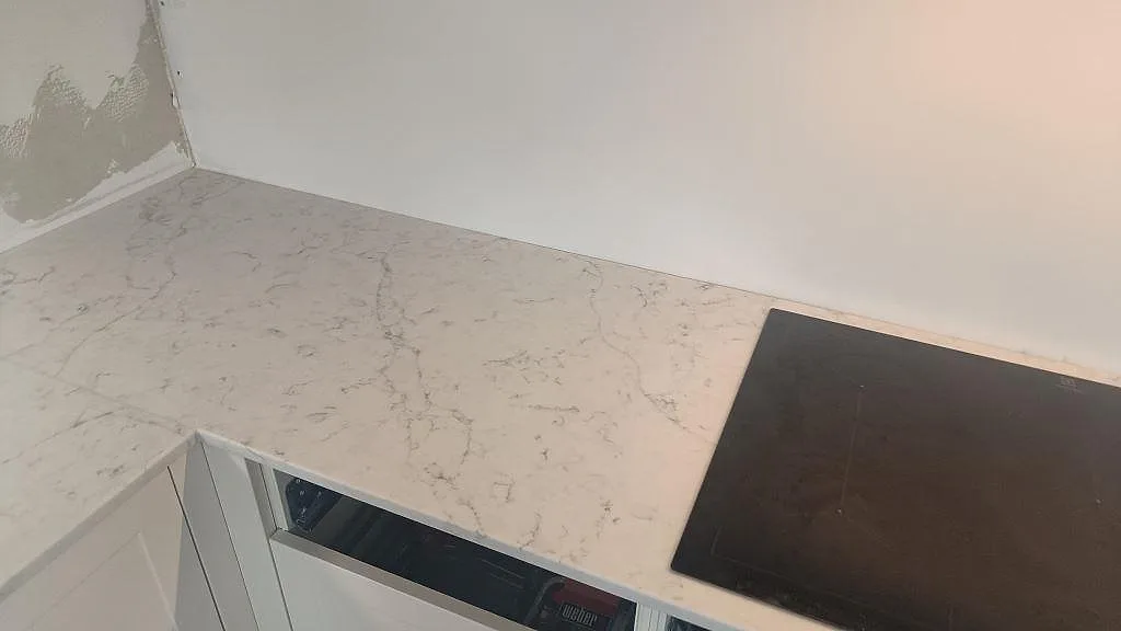 Hörnvy av köksbänkskiva i polerad Technistone Mystery White med grå ådring och hällkant i Bunkeflostrand.