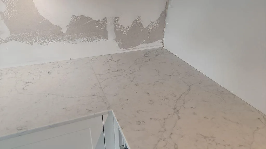 Närbild på hörndel av polerad Technistone Mystery White, med ljus komposityta och ofärdig vägg bakom i Bunkeflostrand.