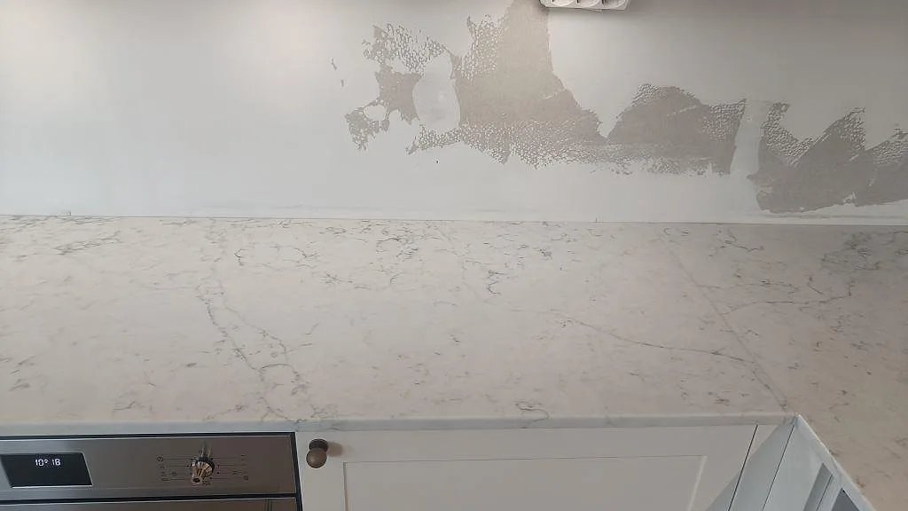 Rak detaljbild av polerad Technistone Mystery White över vita skåp, med grå ådring längs bakkanten i Bunkeflostrand.