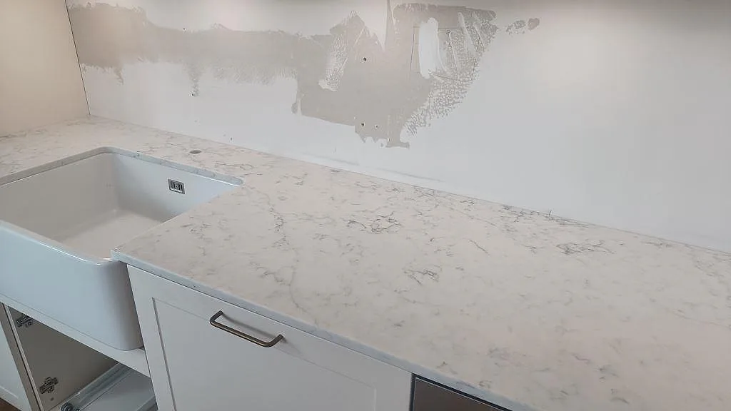 Vinkelbild av köksbänkskiva i polerad Technistone Mystery White, med diskho till vänster och ådrad komposityta i Bunkeflostrand.