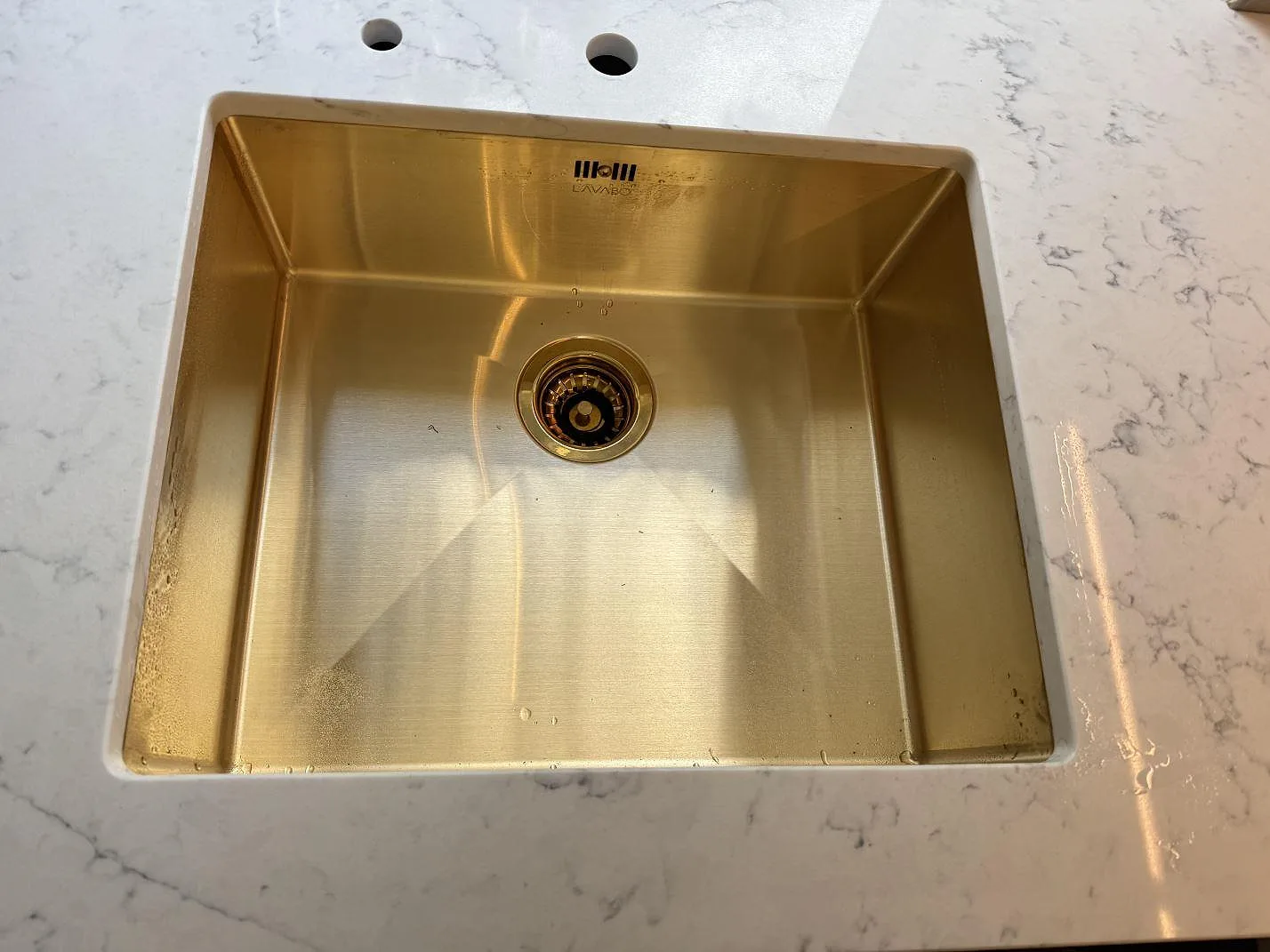Närbild på mässingsfärgad diskho i polerad Technistone Mystery White, vit kvartskomposit med grå ådring i ett kök i Charlottenlund.