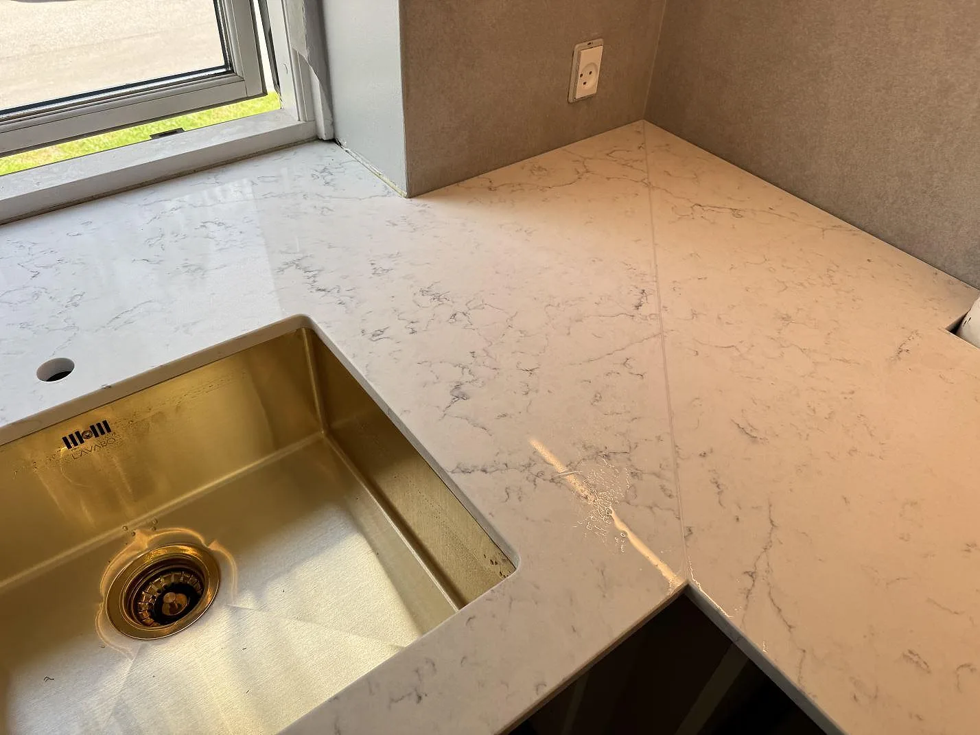 Hörnparti av polerad Technistone Mystery White köksbänkskiva med mässingsfärgad diskho, fönsterljus och ljus komposit i Charlottenlund.