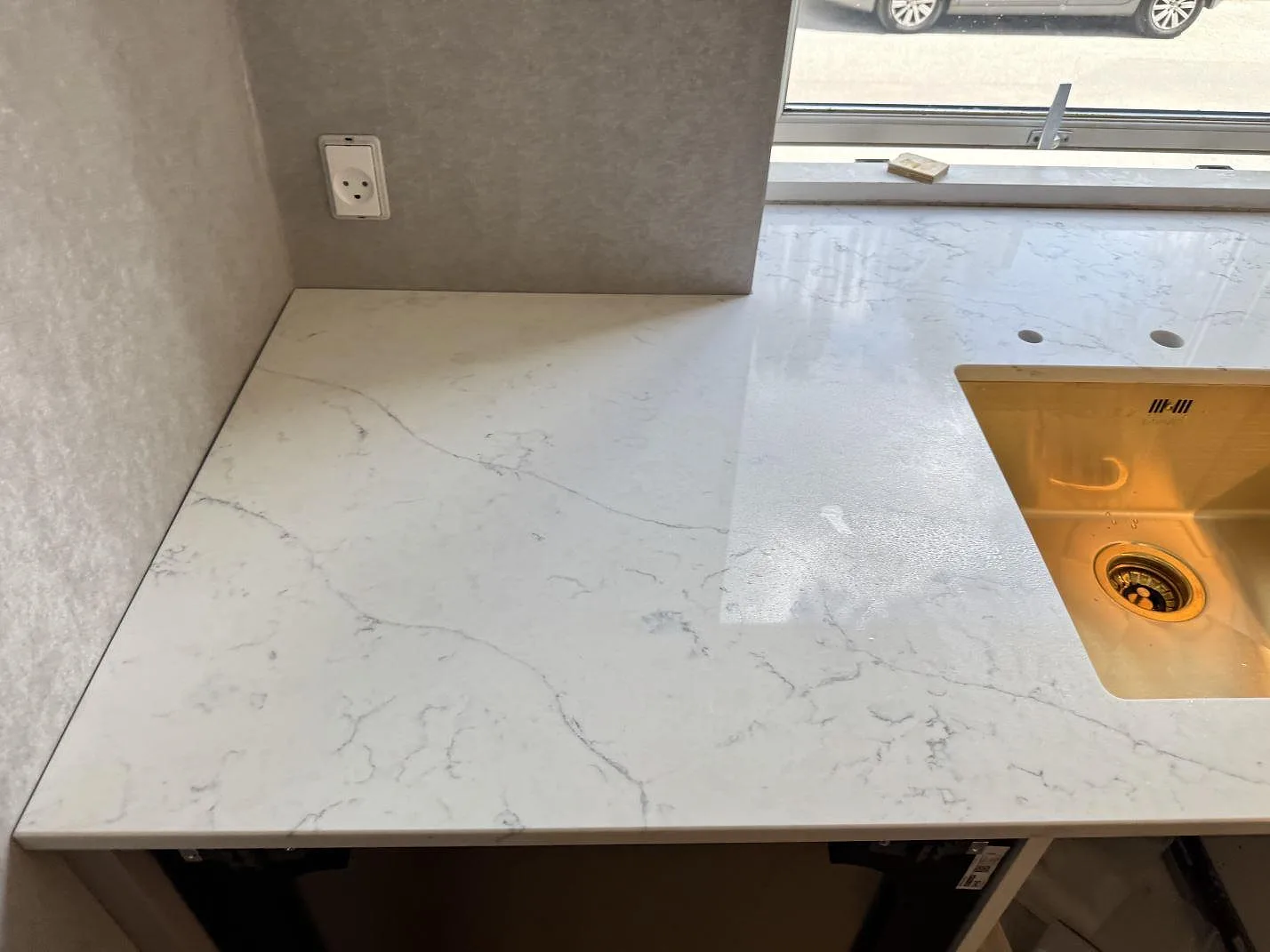 Bred bänkyta i 20 mm polerad Technistone Mystery White med grå ådring, synlig diskho och borrade installationshål i ett kök i Charlottenlund.