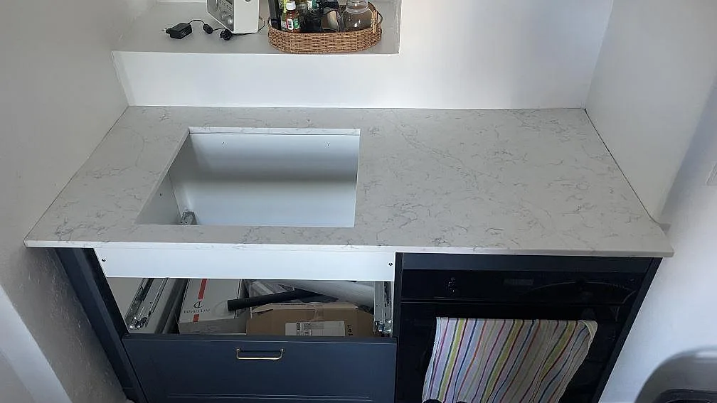 Detalj av polerad Technistone Mystery White köksbänkskiva med rektangulär öppning och öppna lådstommar i Copenhagen.