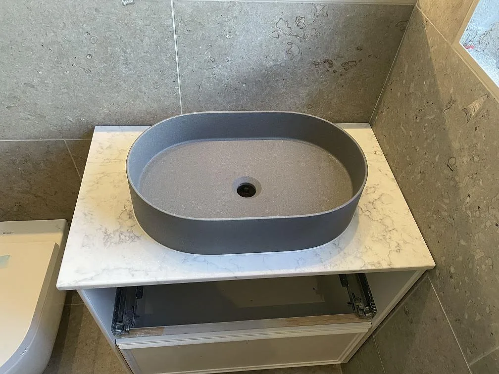 Tvättställsskiva i polerad Technistone Mystery White med ovanpåliggande grått handfat i ett badrum i Djursholm.