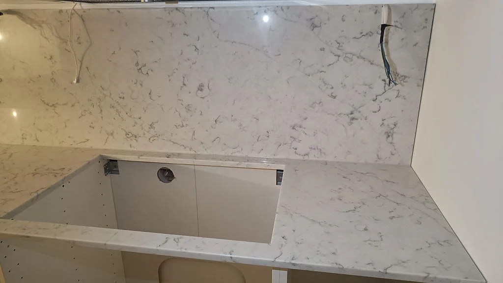 Hörnvy av polerad Technistone Mystery White med bänkskiva, väggskiva och öppna stommar i Falsterbo.