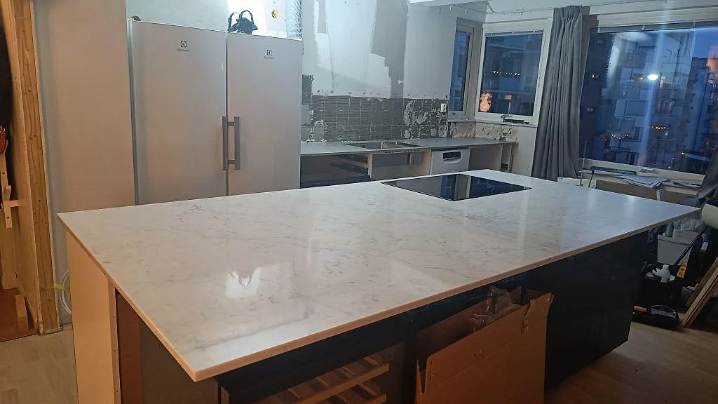 Stor köksö med polerad bänkskiva i Technistone Mystery White kvartskomposit, mörka stommar och häll i ett kök i Göteborg.