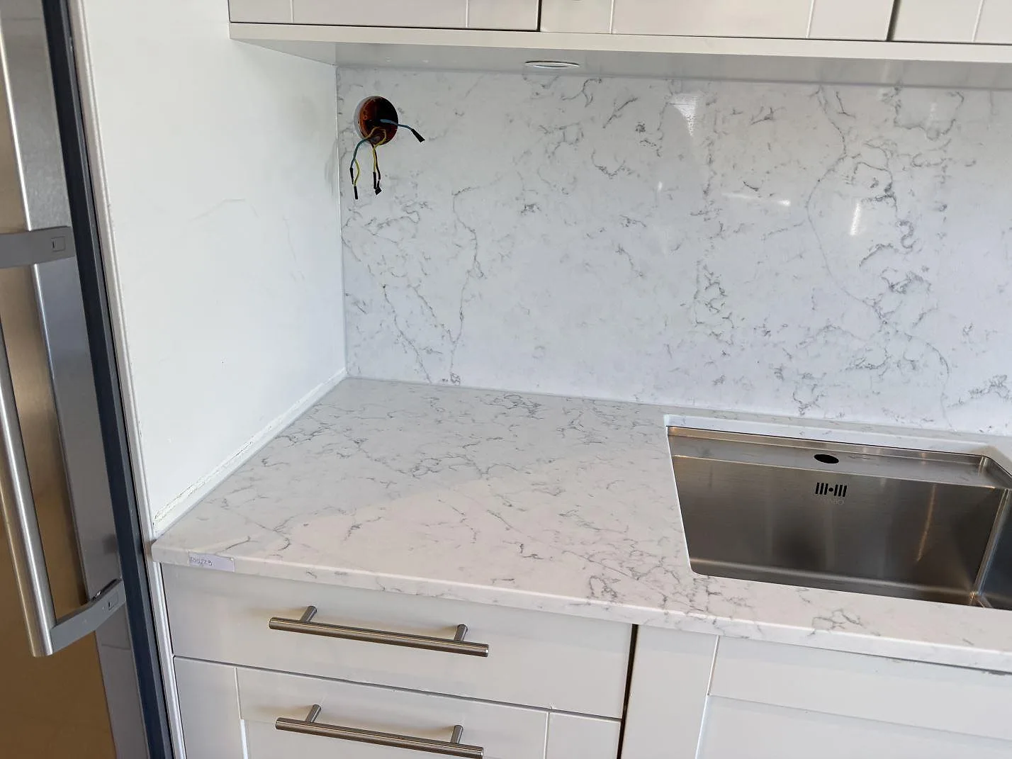 Hörn av köksbänk i vit Technistone Mystery White med uppvikt stänkvägg i samma polerade kvartskomposit, Göteborg.