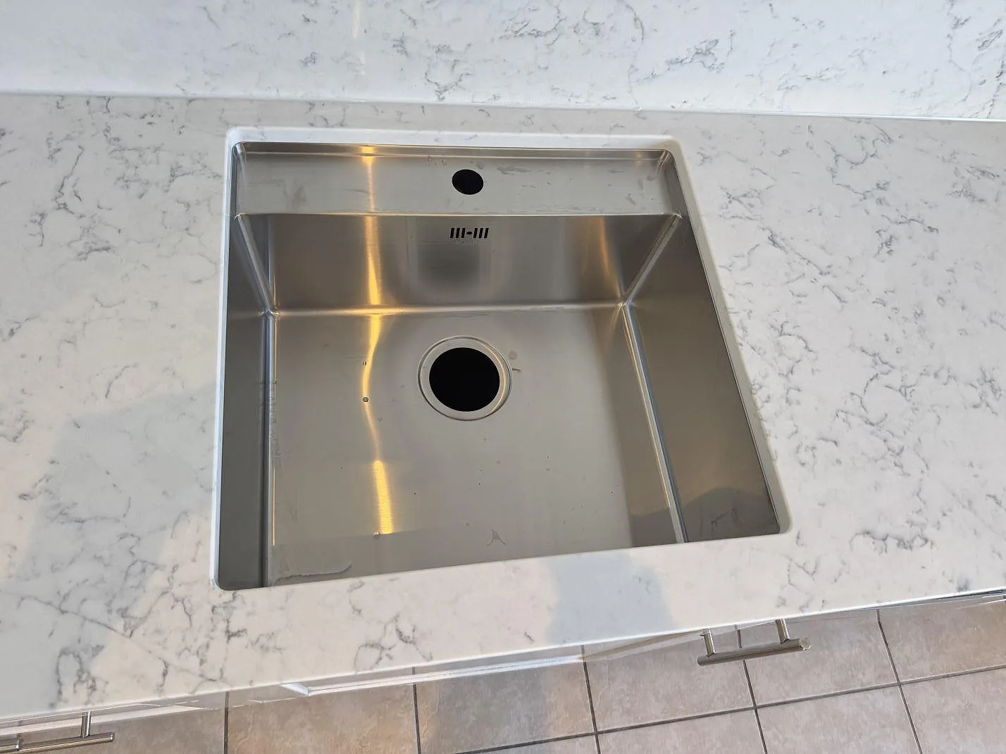 Underlimmad fyrkantig rostfri diskho infälld i polerad Technistone Mystery White-bänkskiva, sedd ovanifrån, kök i Göteborg.