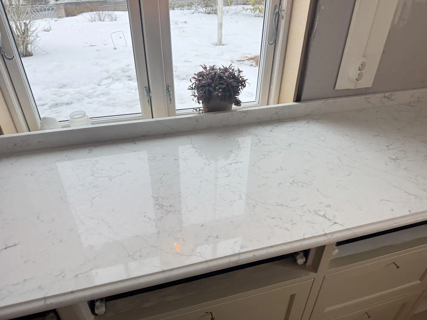 Polerad köksbänkskiva i Technistone Mystery White med grå ådring längs en fönstervänd rad i ett kök i Habo.